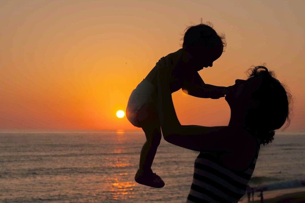 puesta de sol en la playa mujer alzando bebé a contraluz