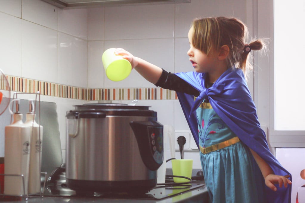niña pequeña cocinando en la olla lenta vestida de princesa
